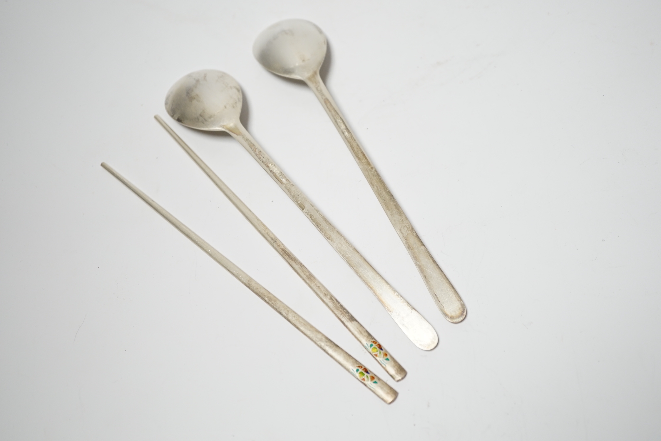 A Korean 990 standard white metal pair of chopsticks, 20cm and two matching spoons with enamelled decoration.
